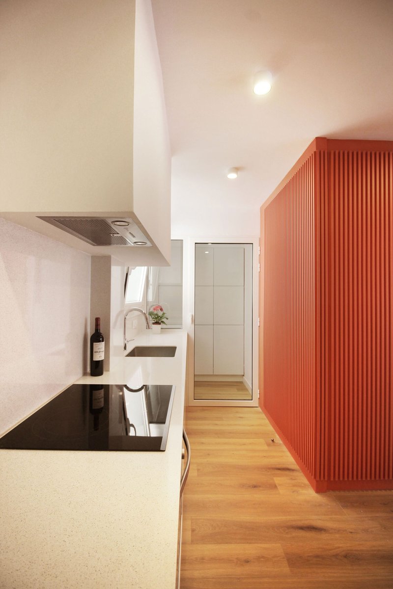 Kitchen counter with integrated cooktop and sink beside a fluted orange volume and wooden flooring