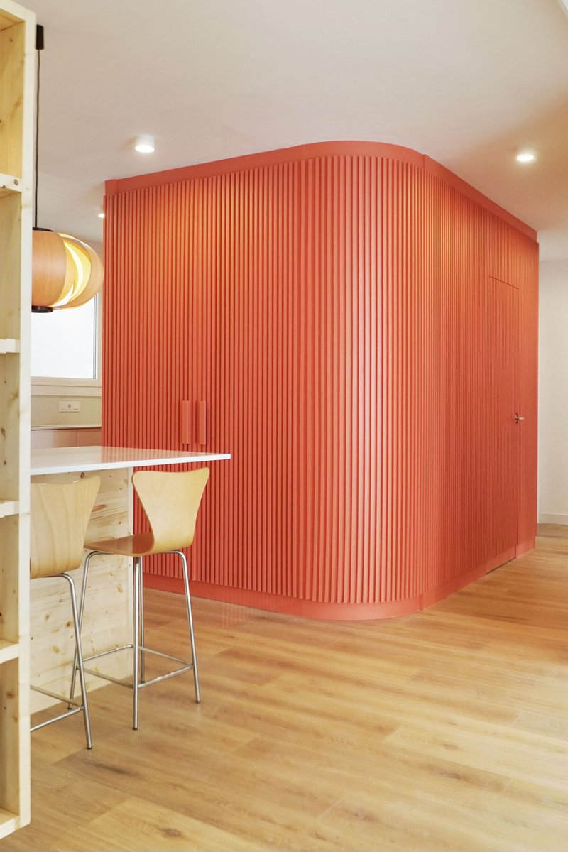 Curved fluted orange volume with breakfast bar and wooden chair under recessed ceiling lights
