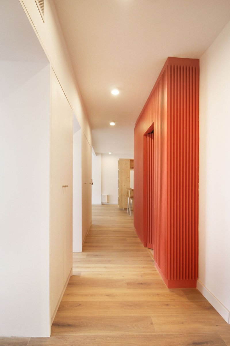 Hallway view along white walls with curved fluted orange volume and light oak flooring