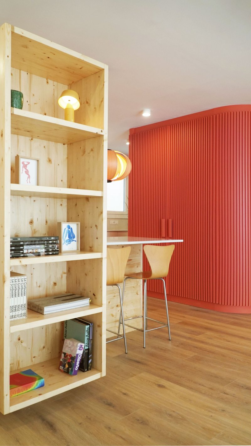 Pine plywood bookshelf beside a red fluted wall panel and a plywood-topped kitchen counter