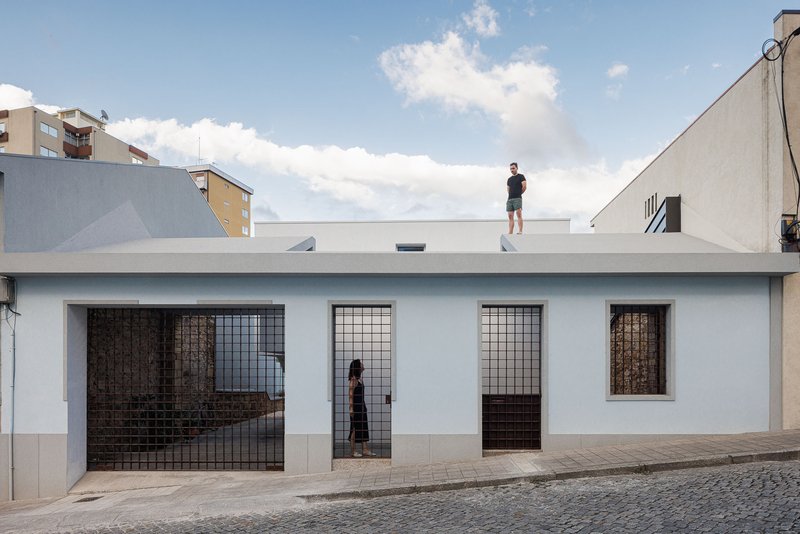 Street facade with white stucco walls and metal grille doors with a figure on the rooftop