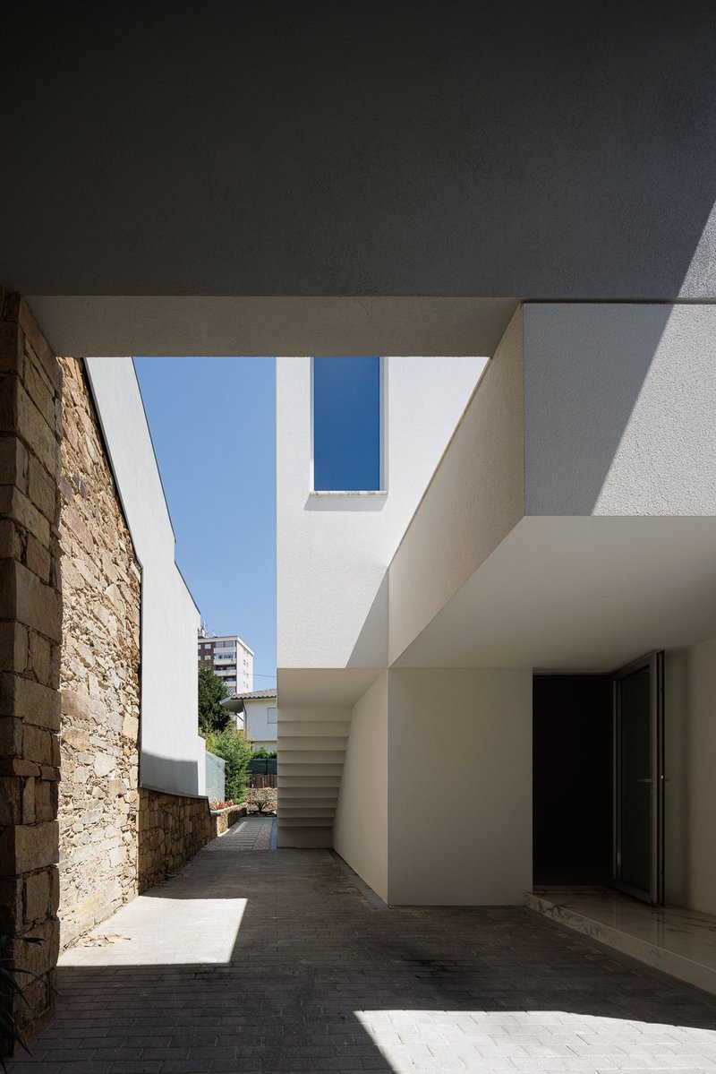 View along courtyard passage showing white volumes, exposed stonework and external stair under blue sky