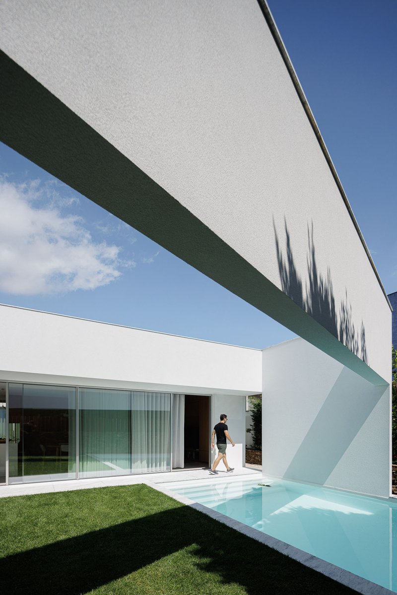 Cantilevered white beam crossing above the pool with person walking past sliding glass doors