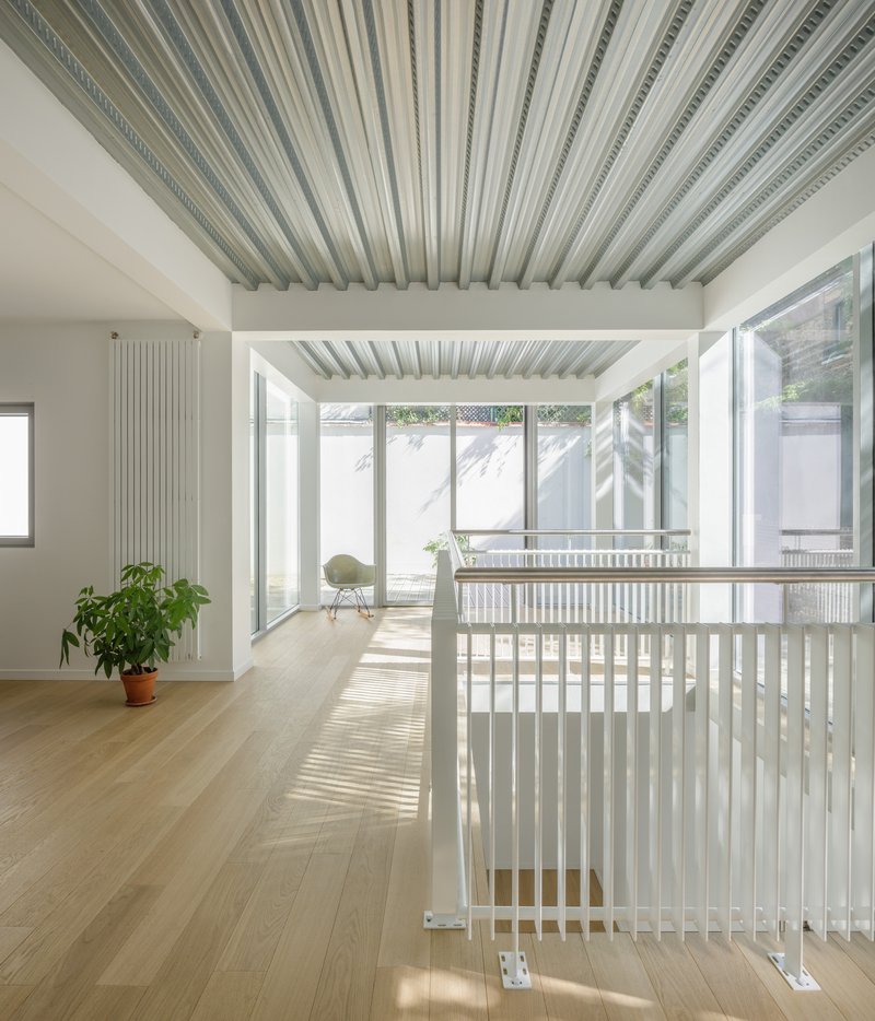 White painted timber balustrade bordering stairwell opening with striped ceiling panels above and courtyard beyond