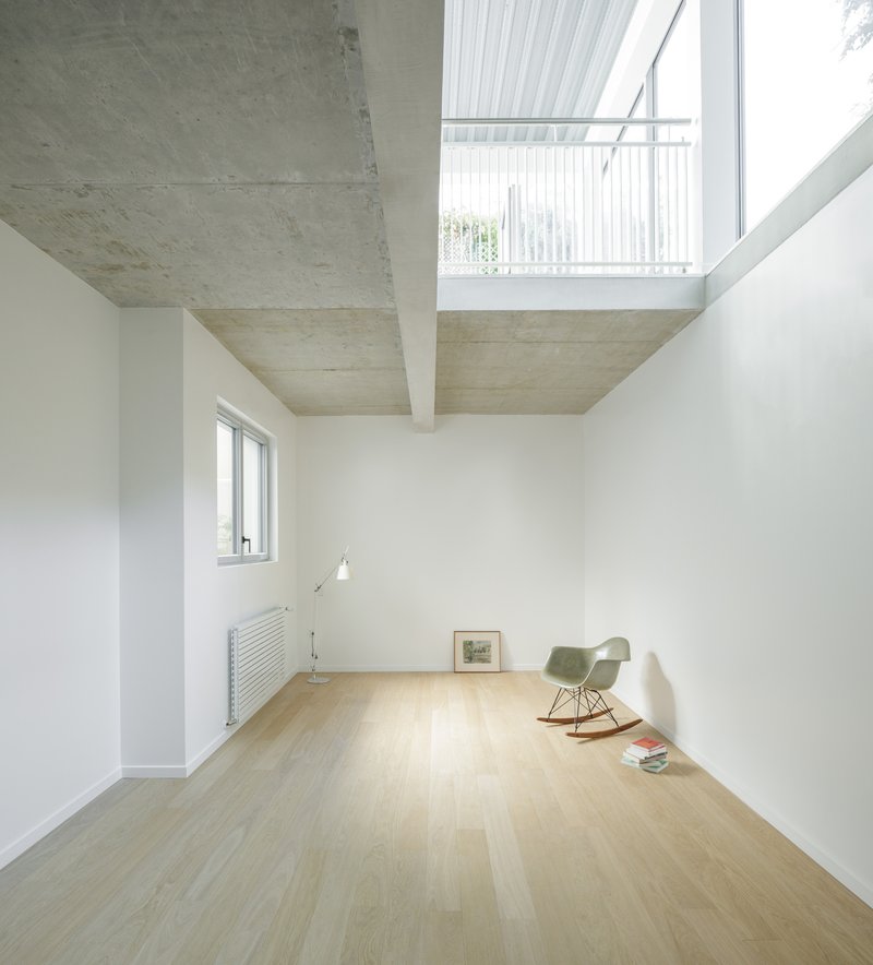 Upper floor room with exposed concrete ceiling beams and clerestory window framing white slat railing above