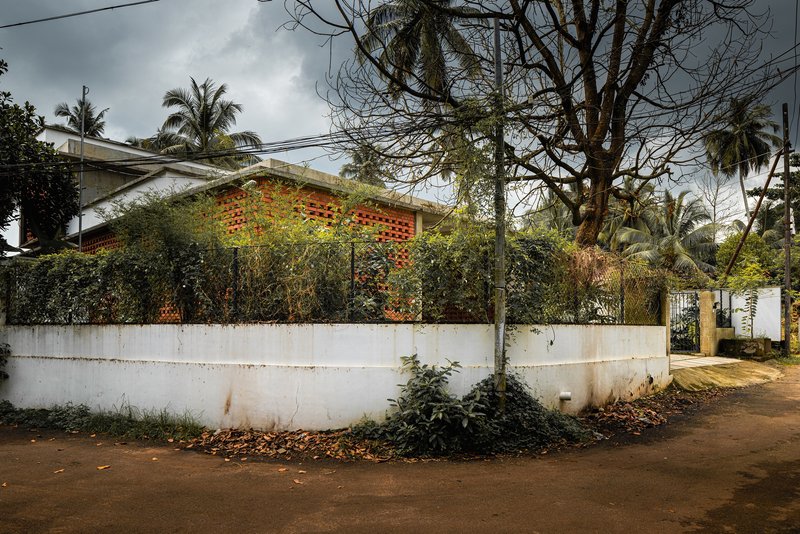 Street view of perforated brick facade behind white boundary wall and leafless tree