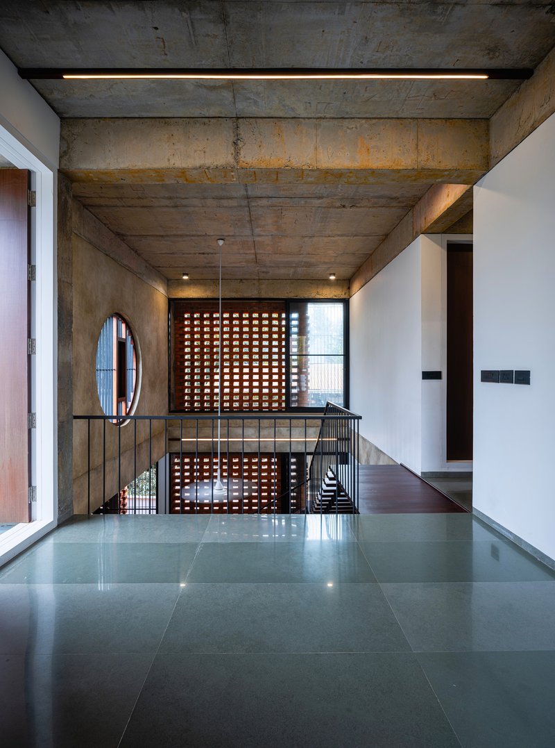 Upper landing with perforated terracotta screen and metal railing under board-formed concrete ceiling