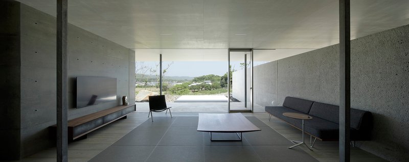 Living space with concrete walls and dark tile floor opening to landscape views through sliding glass