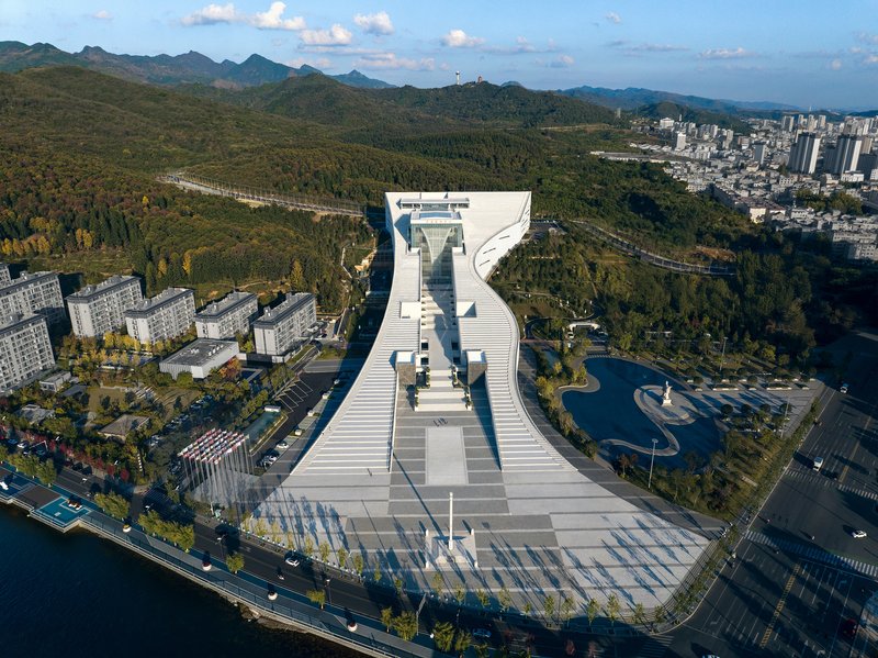Aerial view of the white terraced structure with forested hills and residential blocks in the background