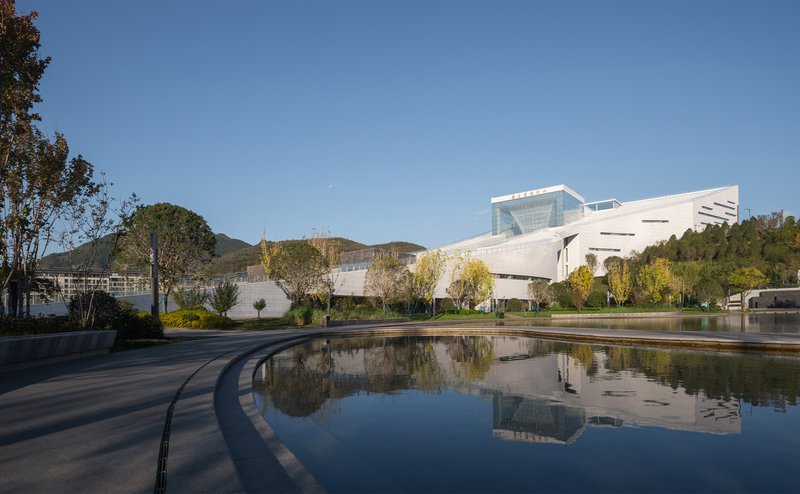 Curved reflecting pool mirroring the white cantilevered volume and surrounding hillside under clear sky