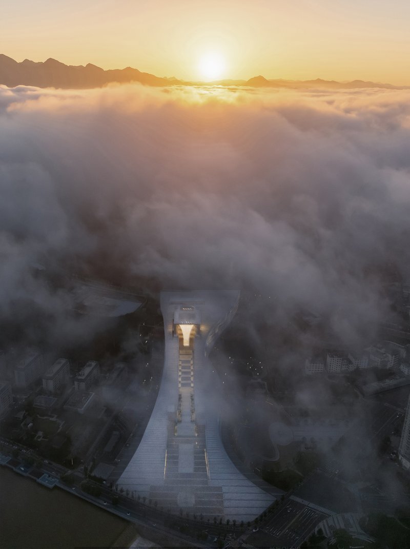 Aerial view of the illuminated monumental plaza and central structure emerging from dense morning fog