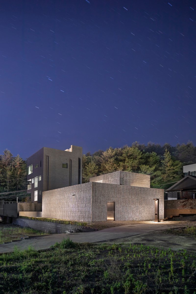 Textured concrete volumes with corner windows photographed under star trails at twilight