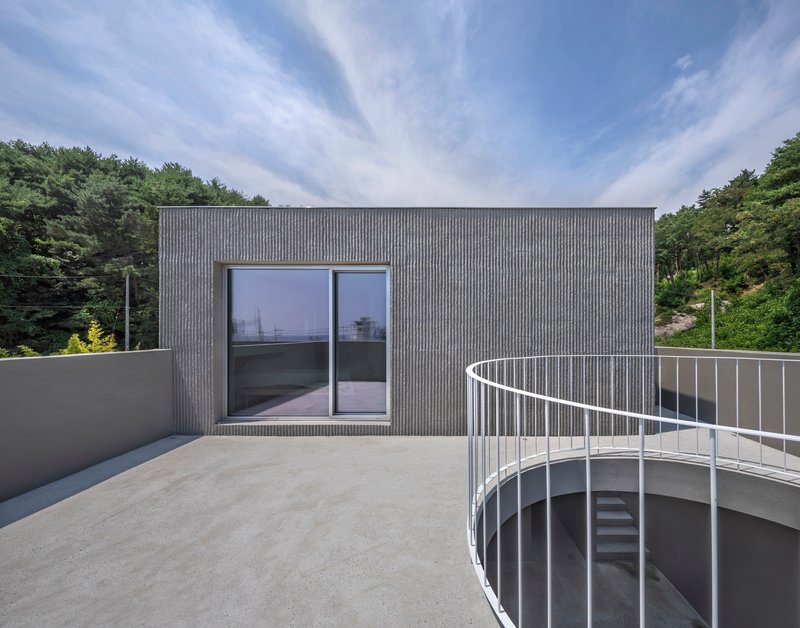 Rooftop terrace with curved metal railing and sliding glass doors against ribbed cladding