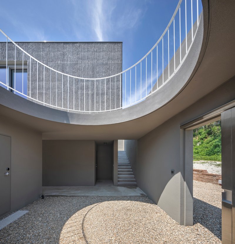 Circular courtyard open to sky with curved railing above and gravel floor below