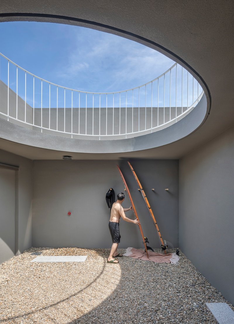 Person adjusting wooden ladder beneath circular skylight in gravel-floored courtyard