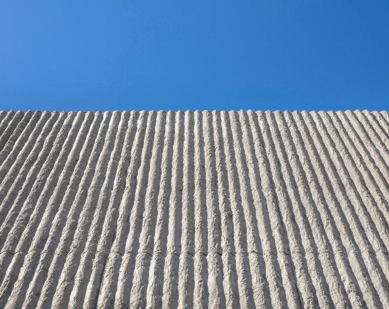 Upward view of ribbed concrete wall surface against a clear blue sky