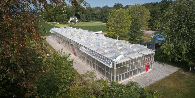 Aerial view of the greenhouse with translucent polycarbonate cladding and sawtooth roof surrounded by trees and lawn