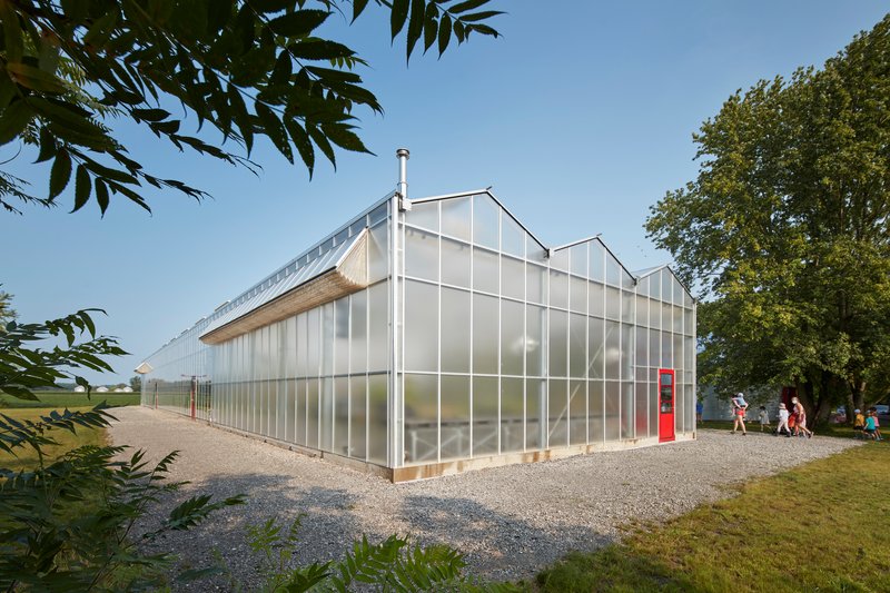 Corner view of the translucent polycarbonate facade with white structural framing and visitors on the gravel path