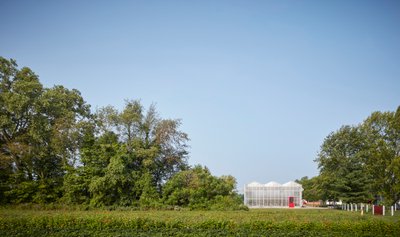 This image showcases a modern greenhouse set within a rural landscape. The greenhouse features a sym
