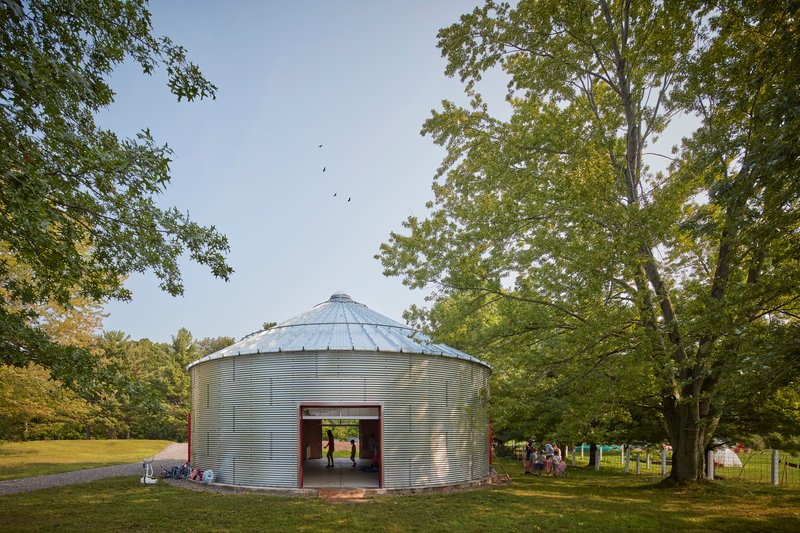 Corrugated metal grain silo repurposed with large red sliding doors opening to views of the surrounding lawn