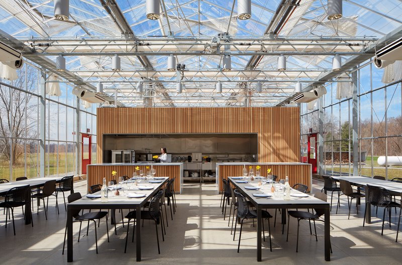 Dining space under an exposed steel truss and glass roof with vertical wood-clad service core