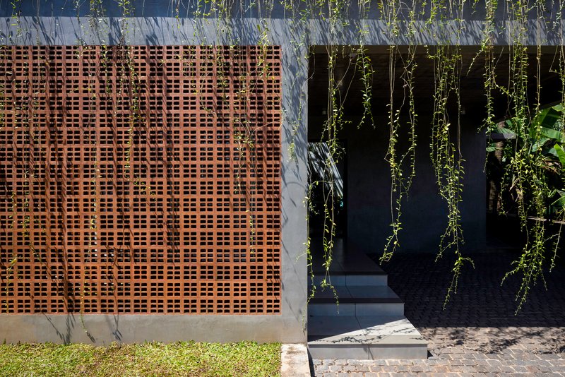 Perforated timber screen beside a dark entrance framed by cascading greenery and lawn edge