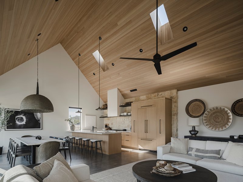 Open living space with vaulted wood ceiling, skylights, stone fireplace wall and pendant lighting over seating