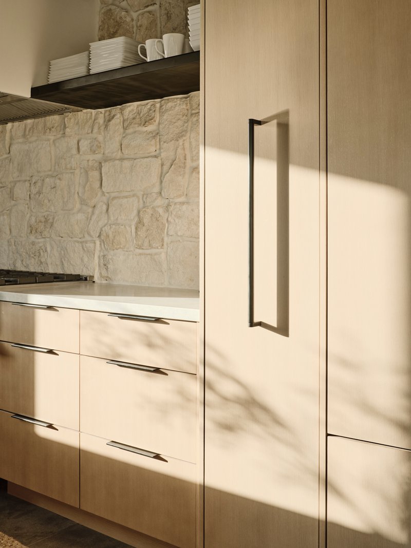 Close-up of light wood cabinetry with vertical bar pulls in afternoon sunlight