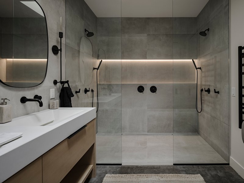 Double shower enclosure with horizontal strip lighting and grey tile walls