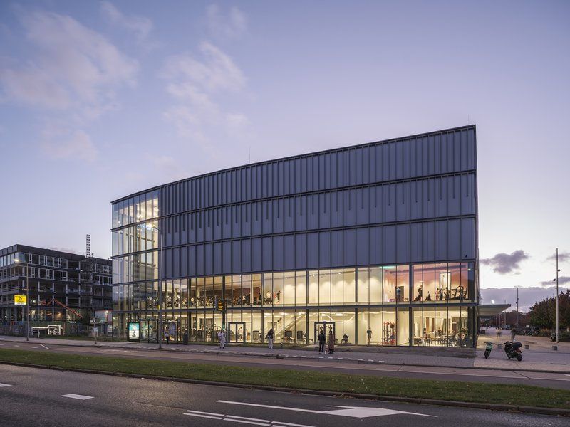 Street-facing elevation with transparent ground floor and ribbed upper stories under evening sky