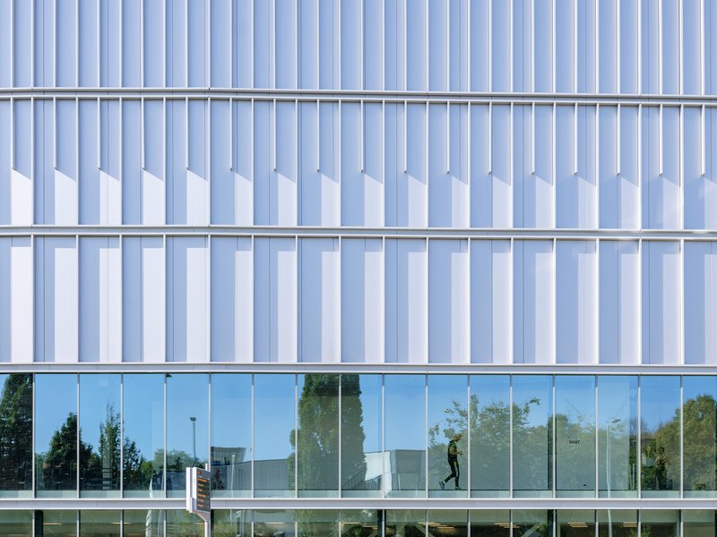 Close-up of vertical metal fins and glass curtain wall with a person walking inside