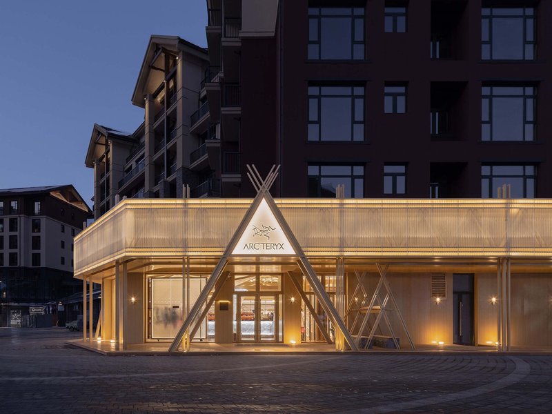 Illuminated translucent facade with triangular timber portal at street level during dusk