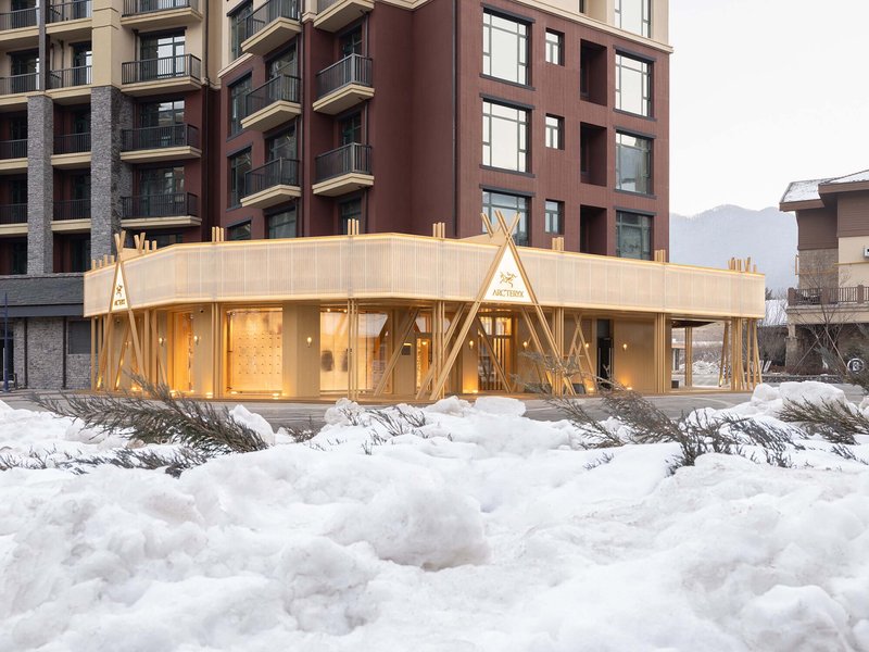 Low-rise pavilion with translucent walls and triangular timber supports surrounded by deep snow