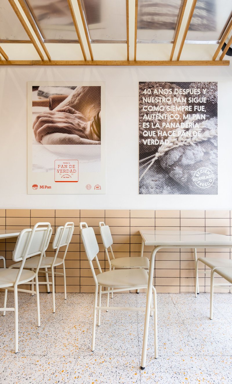 White metal chairs and tables beneath a timber grid ceiling with promotional posters on the wall