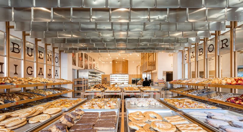 View through the bakery showing timber trays of pastries beneath a woven metal ceiling installation