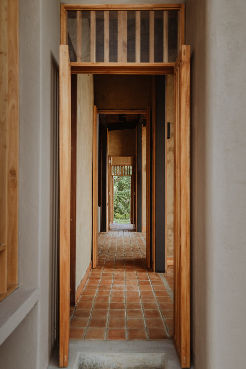 Corridor framed by timber doorways with terracotta tile flooring leading to distant greenery
