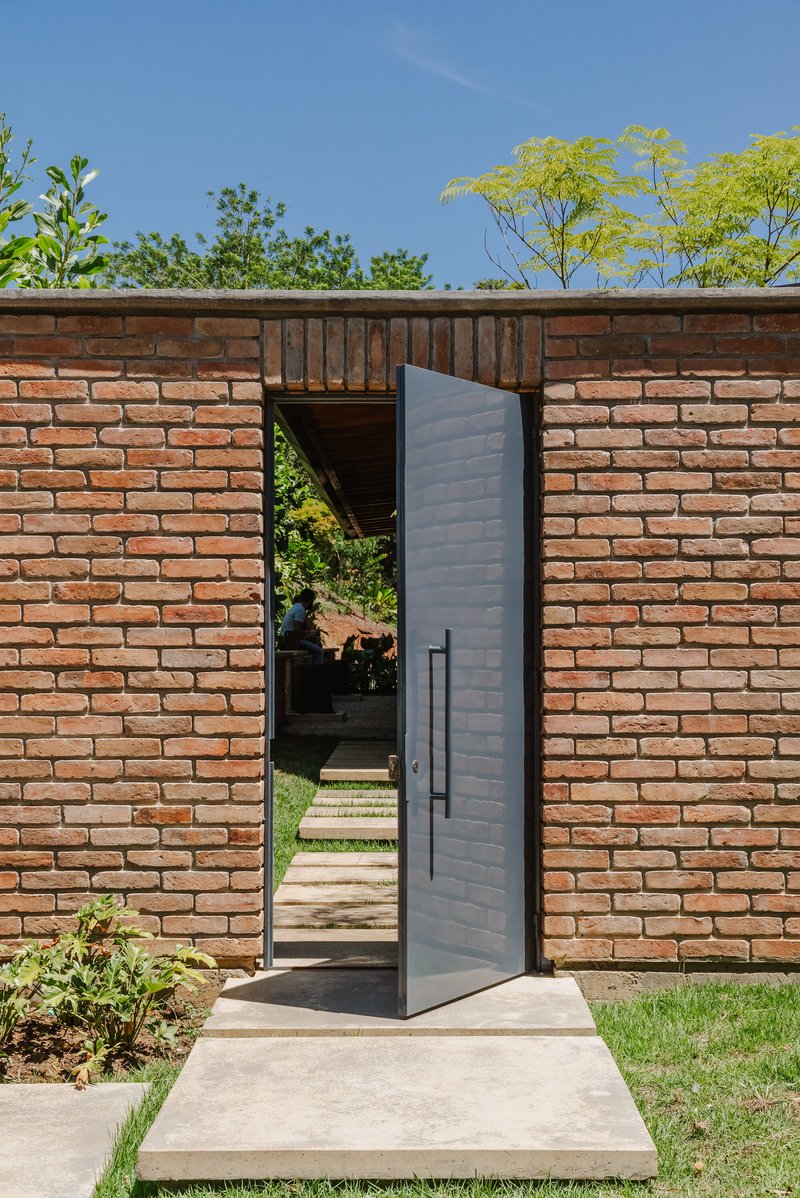 Pivoting black metal door in red brick wall opening to pathway under blue sky