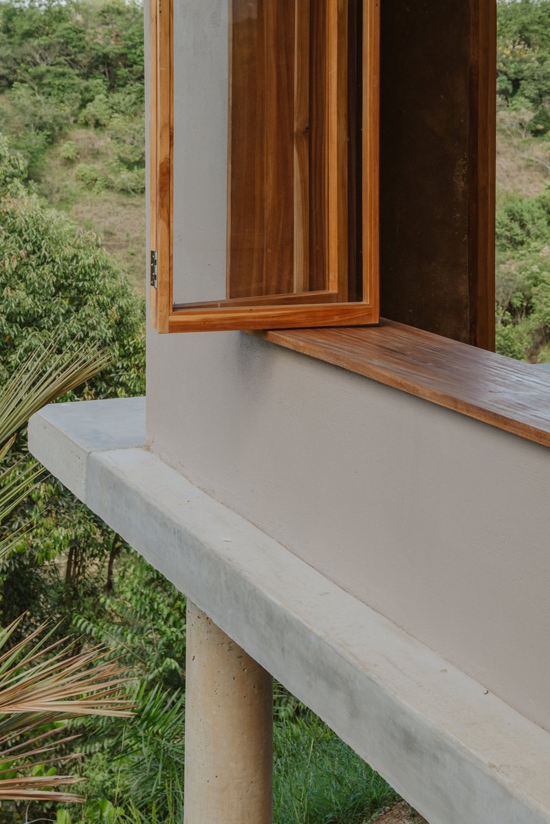 Detail of timber window sill meeting concrete ledge supported by cylindrical column above hillside vegetation