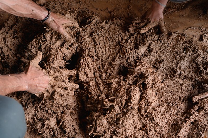 Hands mixing wet clay and straw composite material for wall infill
