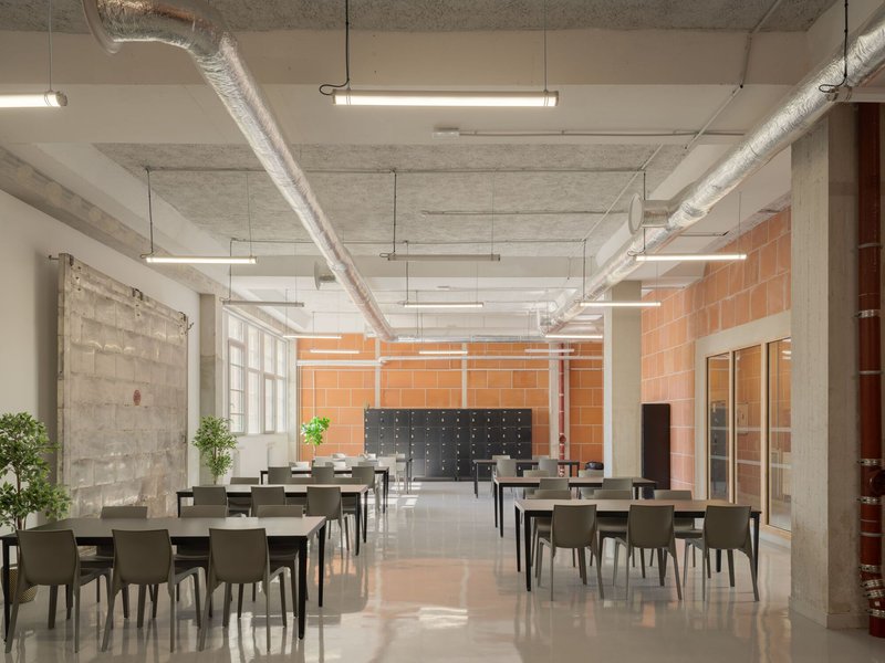 Dining hall with exposed ductwork, concrete columns, terracotta tile walls and rows of tables