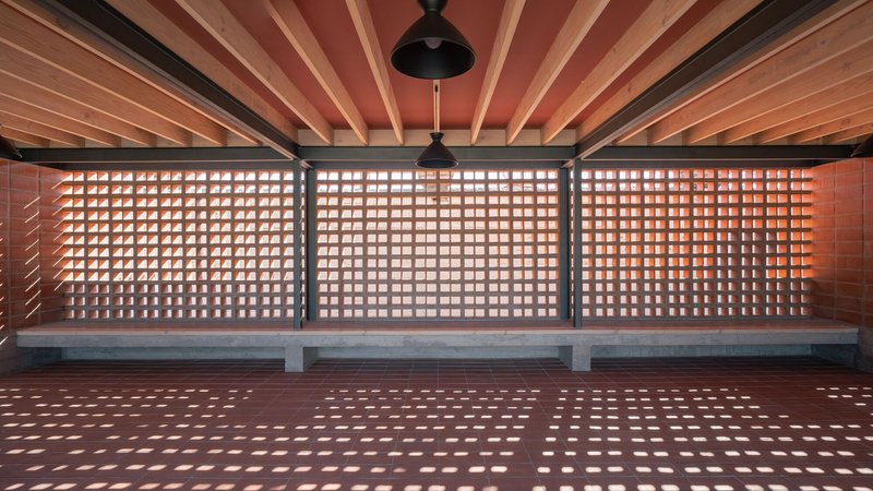 Long view of terracotta screen wall with timber ceiling joists and pendant lights overhead