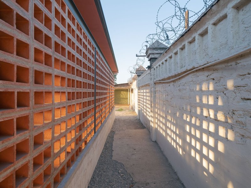 Narrow pathway between terracotta and concrete block walls topped with barbed wire at dusk