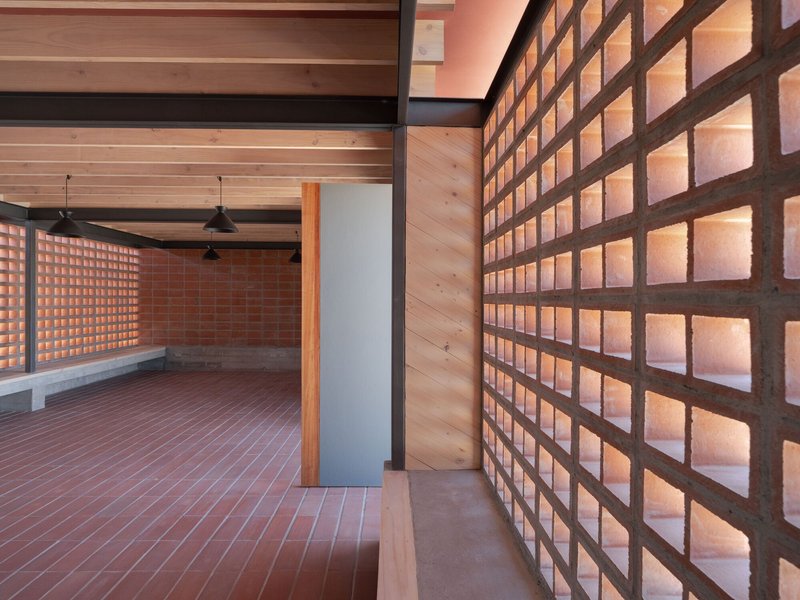 Glowing terracotta block wall alongside timber ceiling and concrete floor with pendant lights