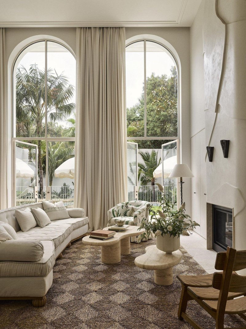 Double-height living room with tall arched windows and curved white fireplace flanked by black sconces