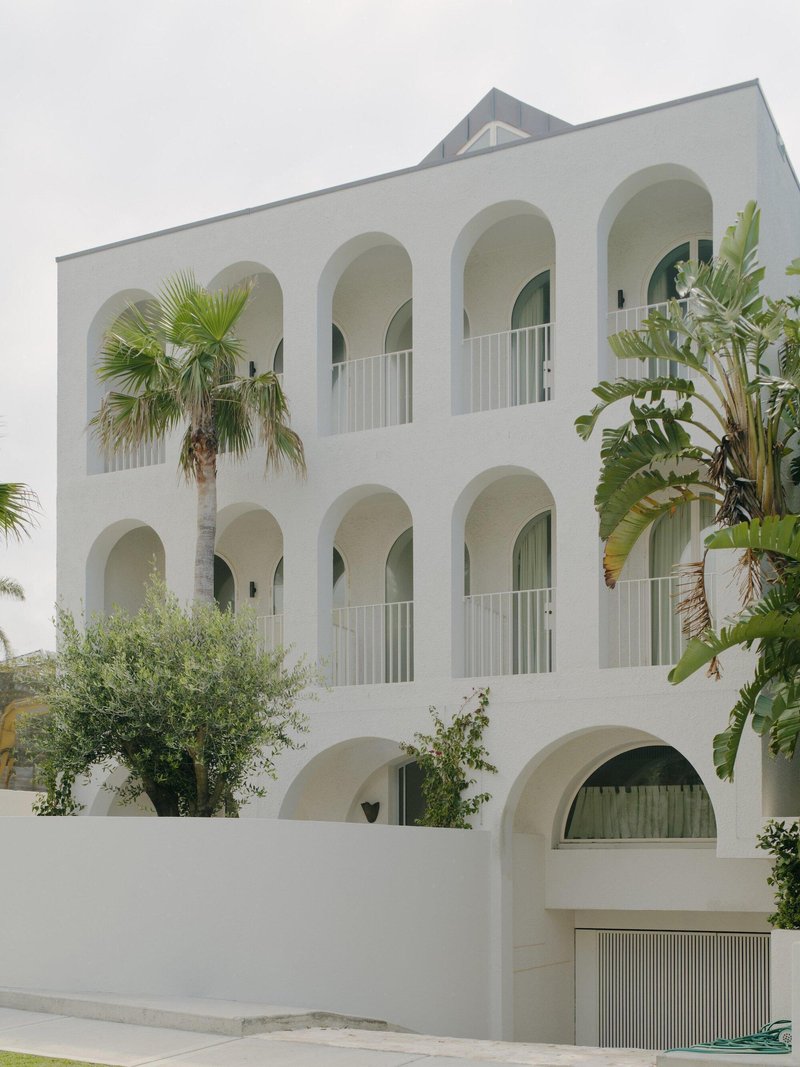 White stucco facade with three tiers of arched openings and balconies flanked by palm trees