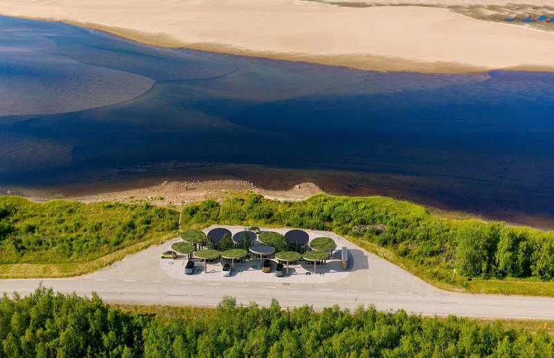 Aerial view of the charging station with circular canopies situated between a coastal road and the blue waterfront