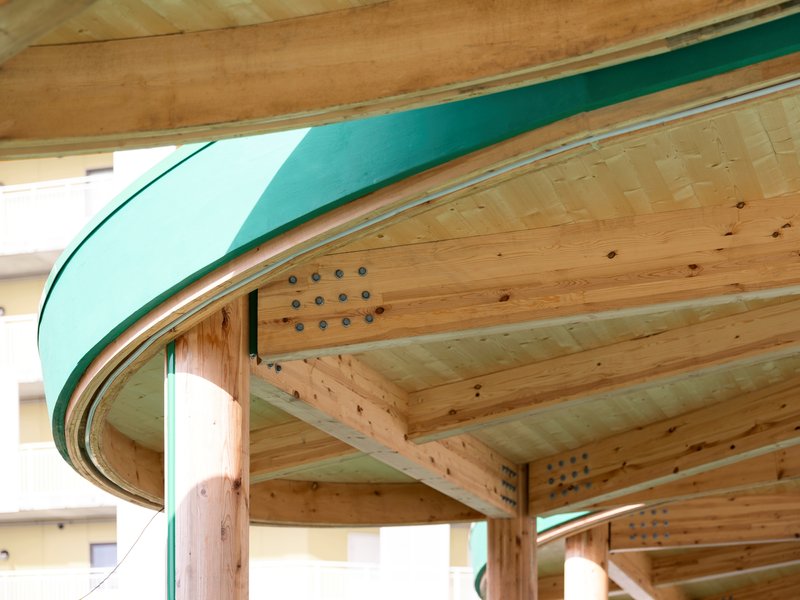 Close-up of the curved timber beams and teal metal edge meeting at the column connection