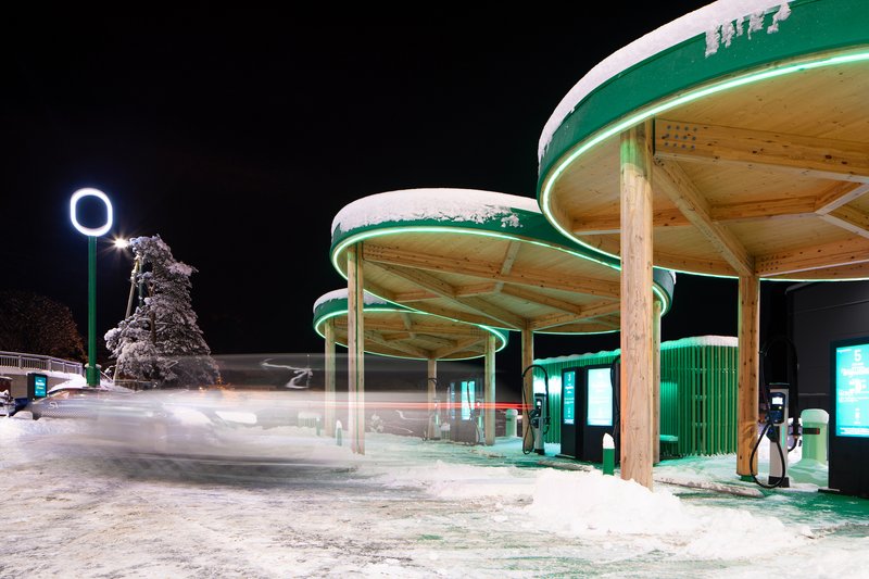 Night view of the illuminated charging station canopies with snow on the ground and a frost-covered tree