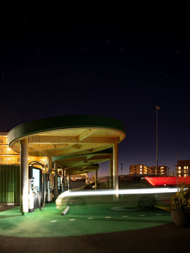 Circular timber canopy over electric charging stations illuminated under a starry night sky