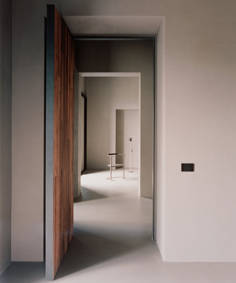 Open timber door revealing a sequence of pale plastered rooms with polished floor